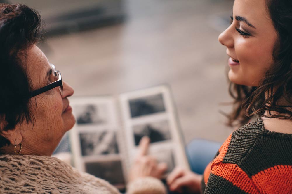 An older woman and a young woman smiling while looking at a photo album, symbolizing family history, generational connection, and the hereditary nature of ADHD.