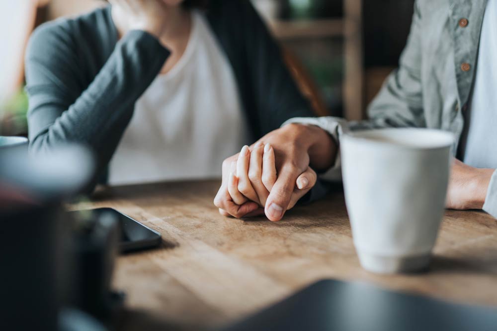 Close-up of couple holding hands at a café table, symbolizing rebuilding trust and accountability in an ADHD relationship.