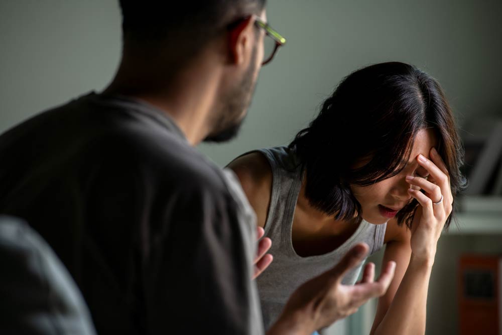 Stressed woman holding her head while partner gestures during an argument, illustrating ADHD-related impulsivity in relationships.