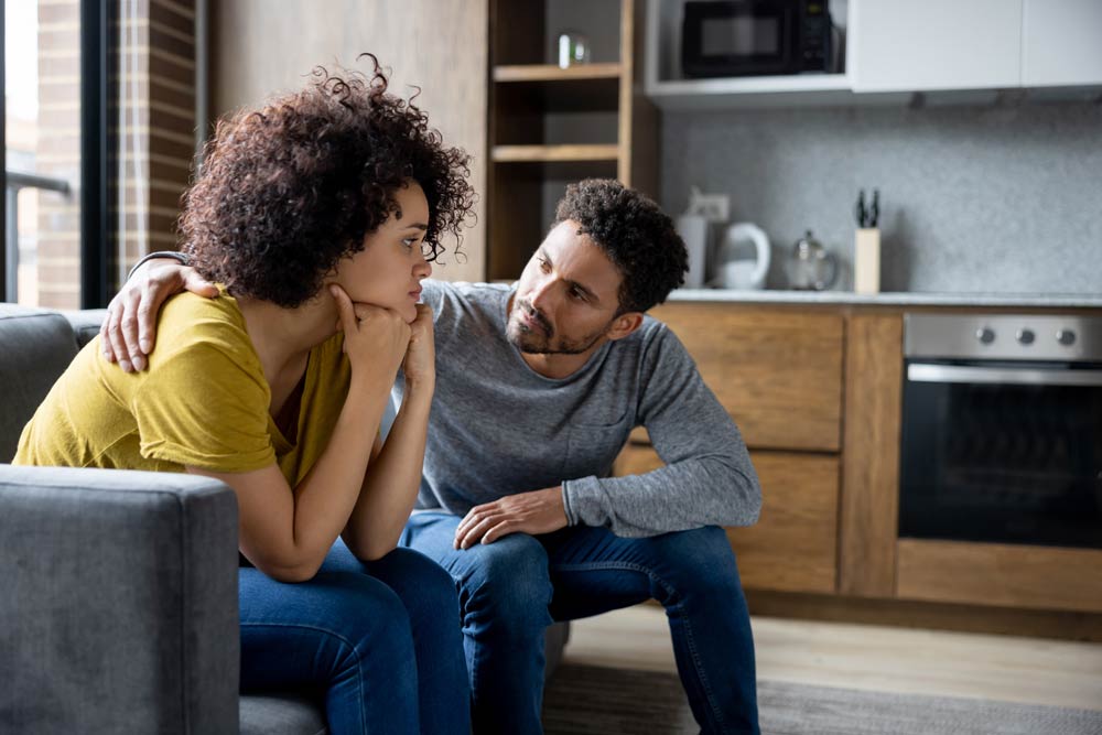 A couple sitting on a couch having an emotional conversation, symbolizing understanding, empathy, and communication in relationships affected by ADHD.