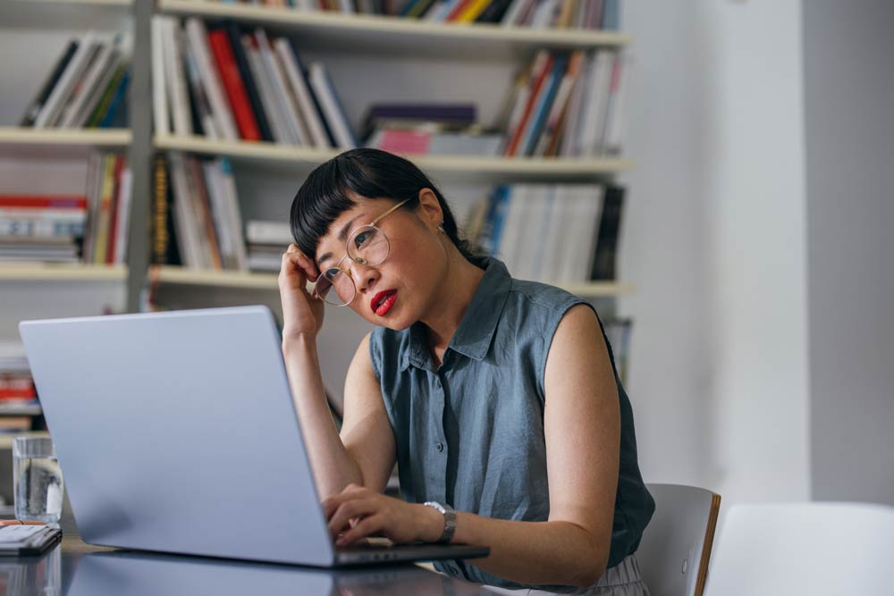 A woman sitting at her desk, looking frustrated while working on her laptop, representing the challenges of emotional regulation and frustration in ADHD.
