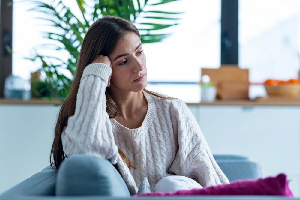 A woman sitting on a couch looking thoughtful and pensive, symbolizing the emotional regulation challenges experienced by individuals with ADHD.