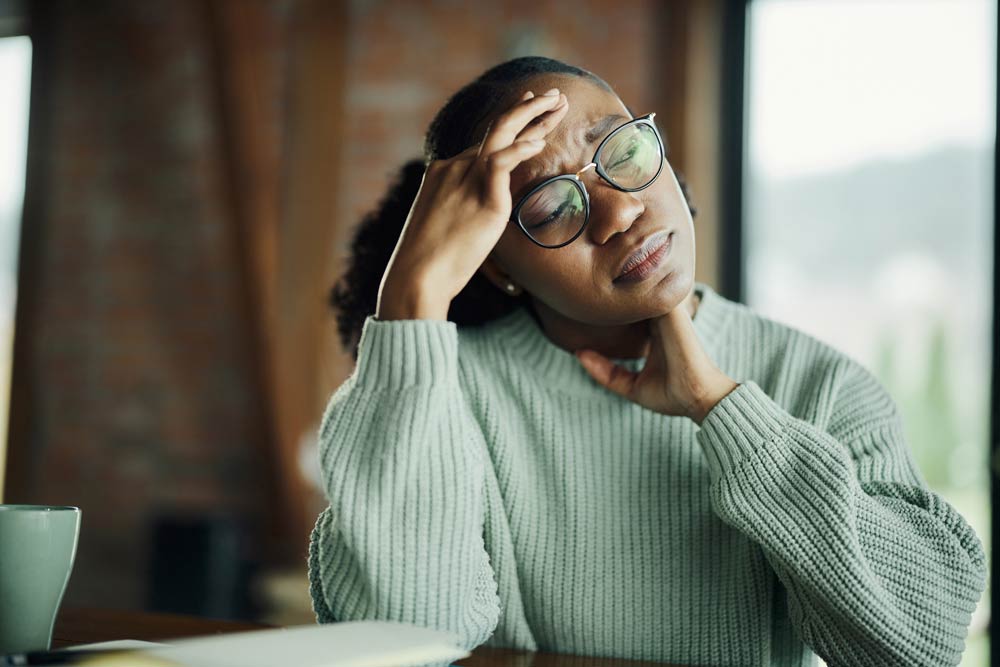 A woman holding her head in frustration at a desk, representing the stress, overwhelm, and emotional fatigue often experienced by adults with undiagnosed ADHD.