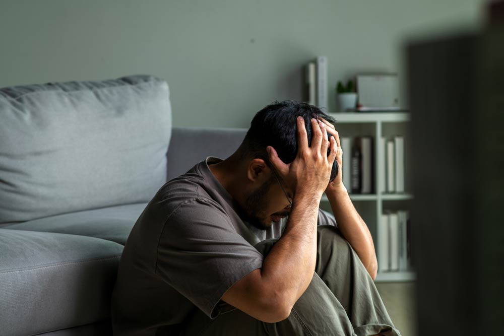 A man sitting on the floor with his head in his hands, expressing frustration and overwhelm, symbolizing the emotional and mental challenges faced by men with ADHD.