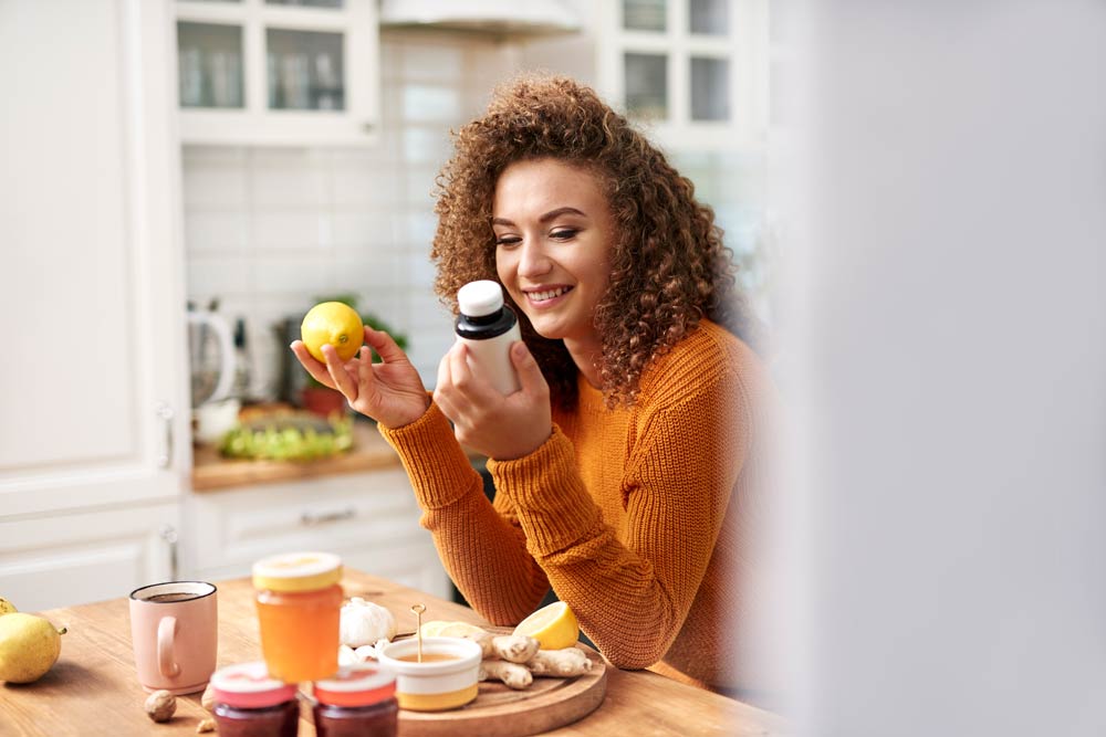 A woman smiling while holding a supplement bottle and a lemon in her kitchen, symbolizing thoughtful consideration of natural and nutritional approaches to managing ADHD.