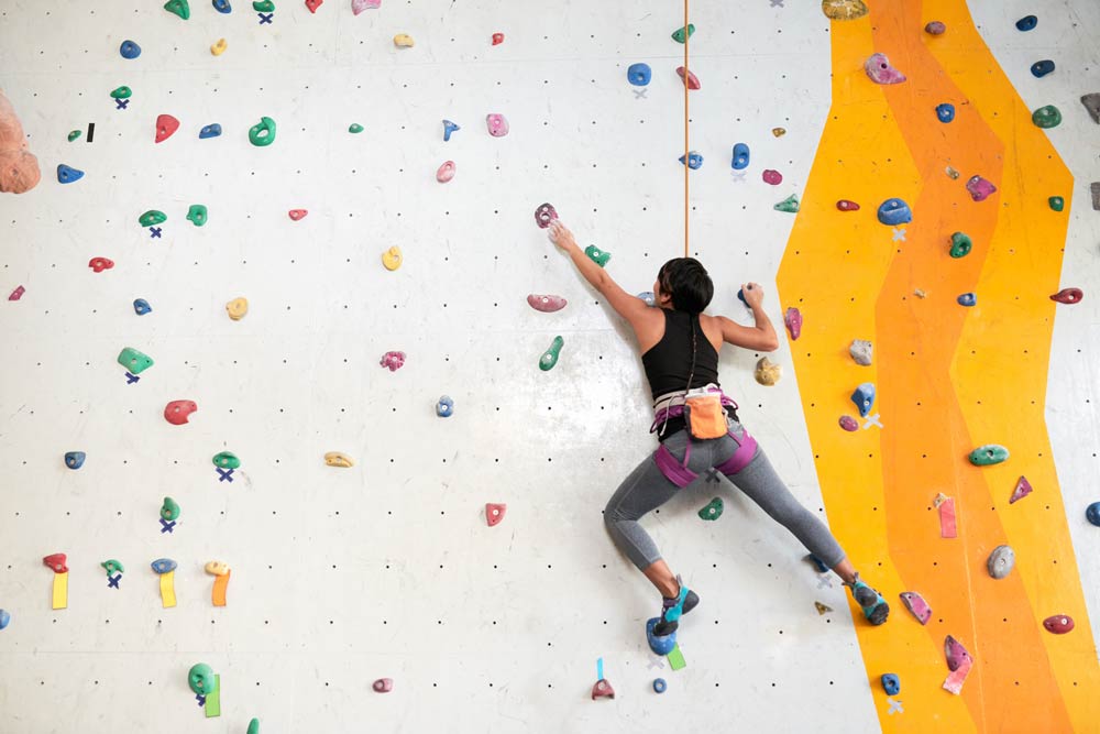 A woman rock climbing on an indoor wall, representing the focus, energy, and engagement that come from ADHD-friendly physical hobbies.