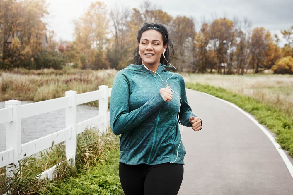 A woman jogging outdoors in a park, wearing earphones and a teal jacket, symbolizing how regular exercise improves focus, attention, and emotional regulation in ADHD.