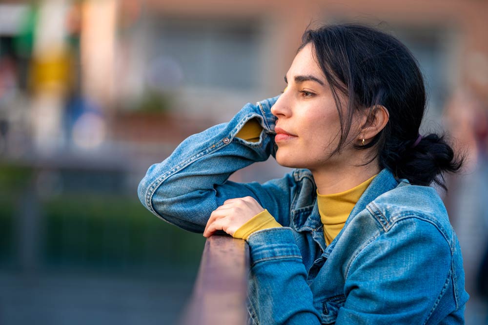 Woman in a denim jacket gazing thoughtfully into the distance, representing reflection and emotional regulation through therapy for ADHD.