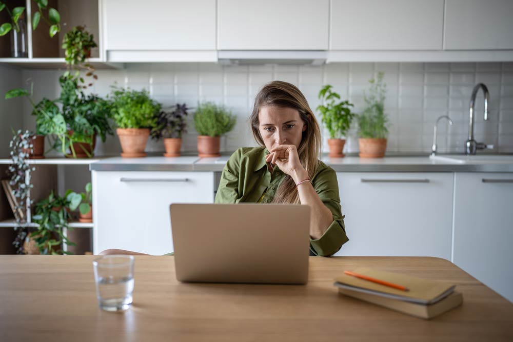 Woman working on a laptop at a kitchen table, representing the challenges of career planning with ADHD.