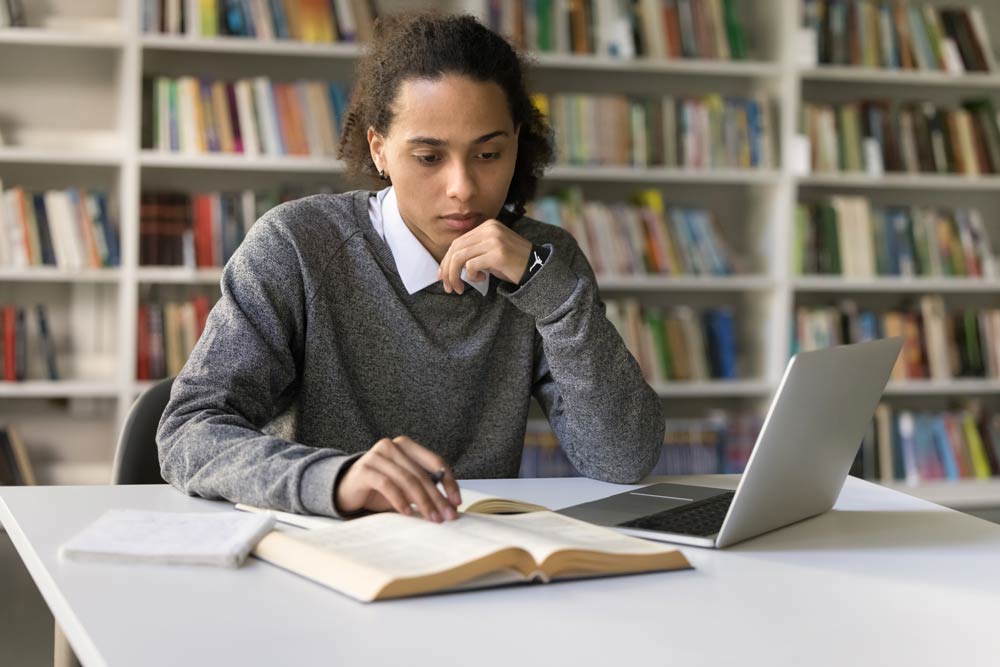 Focused young adult studying in a library with books and a laptop, representing ADHD strengths in career exploration.
