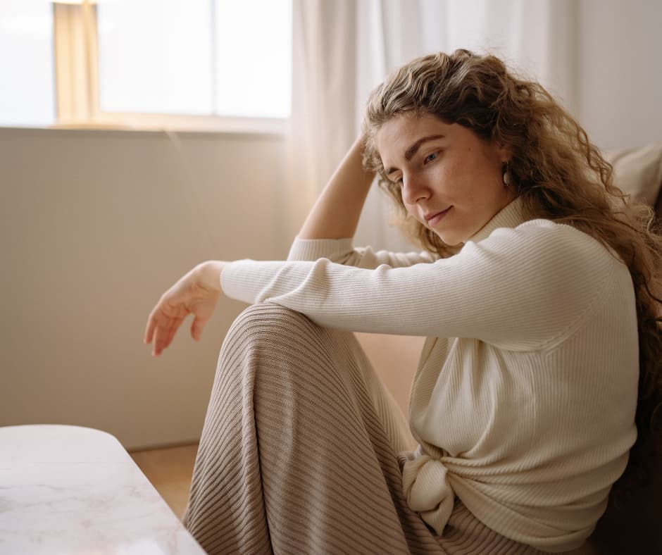 Nachdenkliche Frau sitzt alleine auf einem Sofa und denkt über ihre Beziehung, Unsicherheit, Vertrauen und mögliche Veränderungen ihres Partners nach
