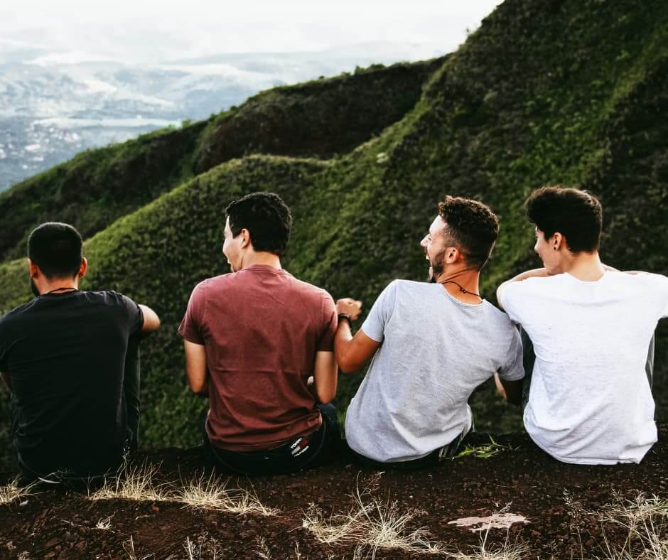 Vier Männer sitzen gemeinsam auf einem Hügel und geniessen die Aussicht – Symbolbild für Freundschaft, Nähe, Verbundenheit und Männerfreundschaften