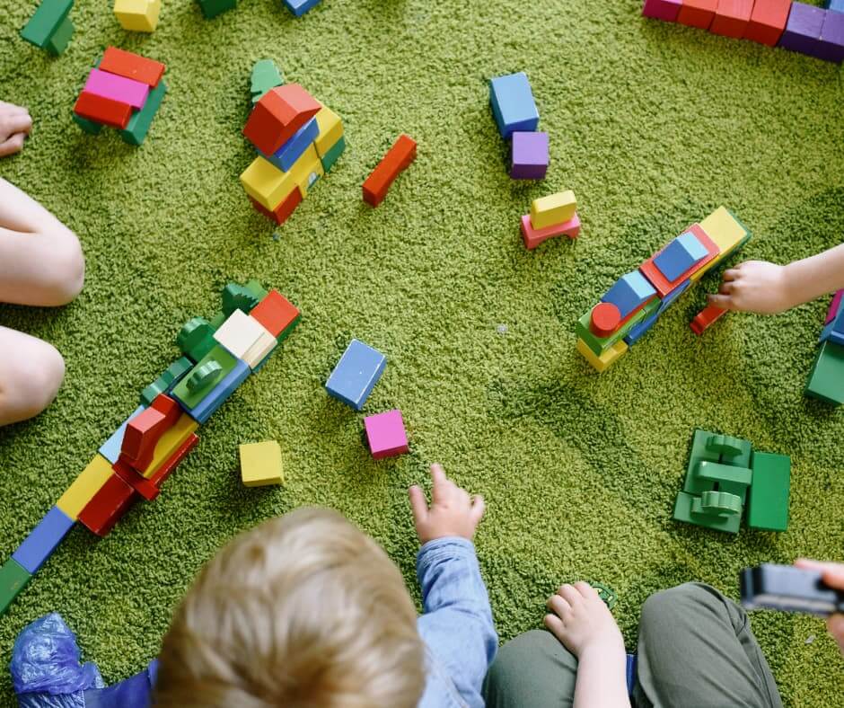 Kinder spielen gemeinsam mit bunten Bauklötzen auf einem Teppich. Symbolbild für Familie, Kinderwunsch und die Frage nach Elternschaft.