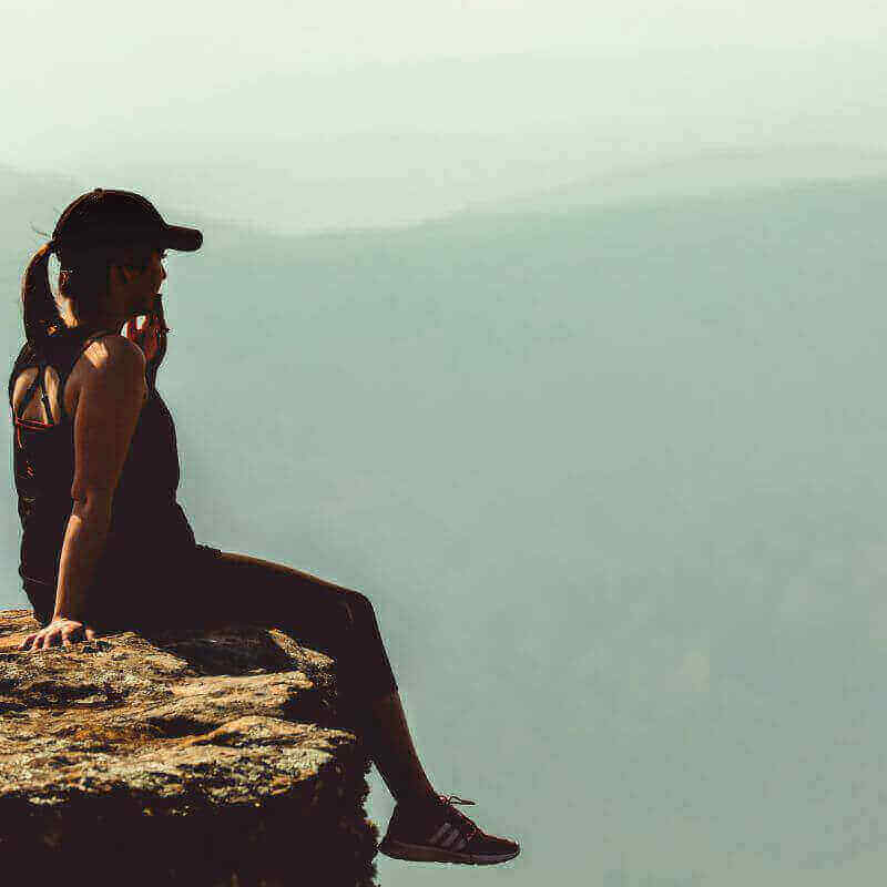 Frau sitzt nachdenklich am Meer und blickt in die Ferne – Symbolbild für zyklisches Arbeiten, Selbstreflexion, Energie und den weiblichen Menstruationszyklus