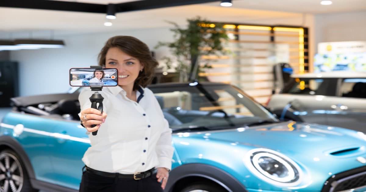 Sales rep filming a personalized vehicle walkaround video on a smartphone in a car showroom
