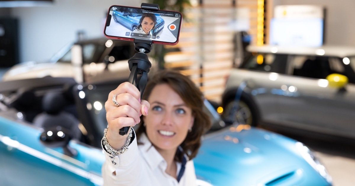 A car sales rep recording a personalized walkaround video on a smartphone gimbal in a dealership showroom, the first step in a fast speed to lead workflow