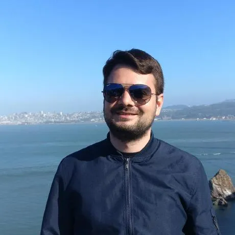 A person in sunglasses stands by a scenic waterfront, with a city skyline in the background.