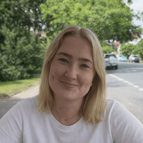 Smiling woman in white t-shirt outdoors with tree-lined street background