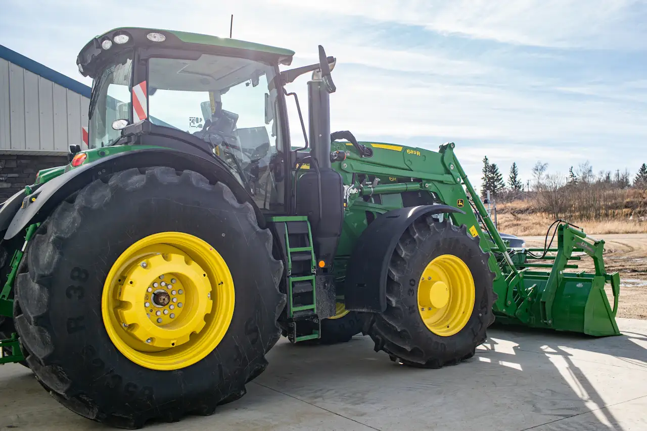 Agricultural equipment repair on a John Deere tractor with a front loader outside a heavy-duty service shop.