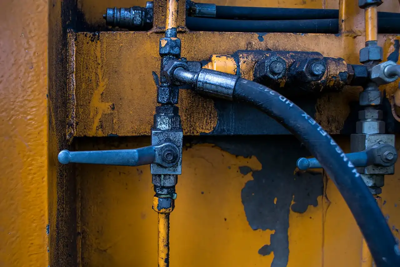 Hydraulic repair service for heavy-duty equipment, showing worn hoses, control valves, fittings, and fluid-stained components.