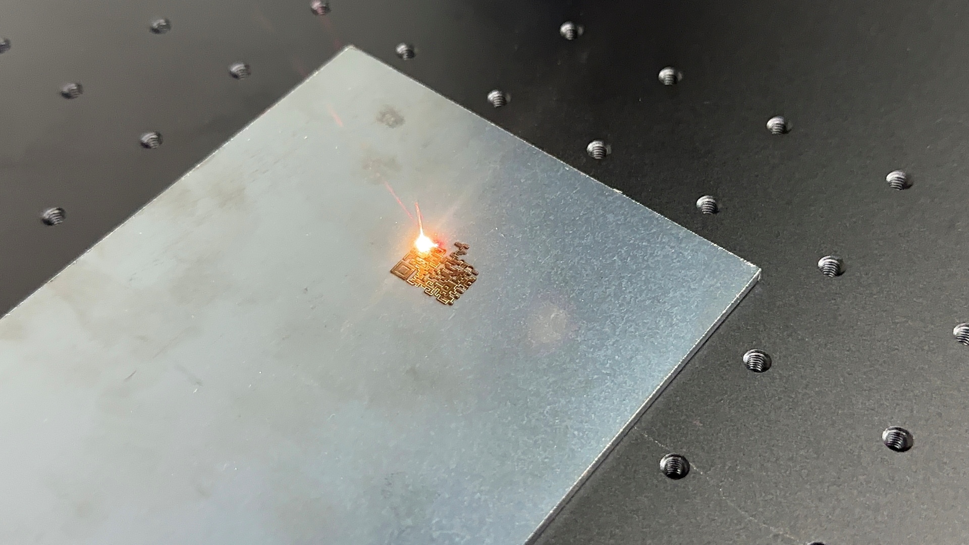 Gravação de QR code a laser sendo feita em placa de metal.