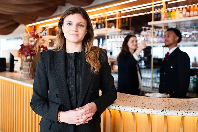 une manager de l'hôtellerie restauration qui pose devant un bar / réception