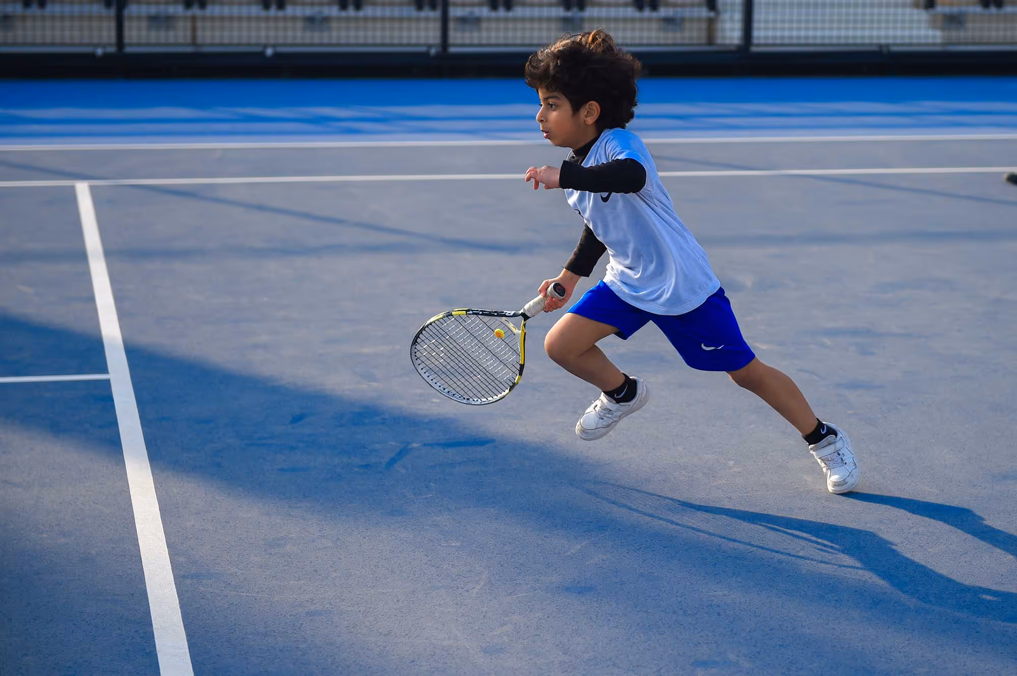 a Kid playing tennis on a blue tennis court at Rafa Nadal Academy Kuwait