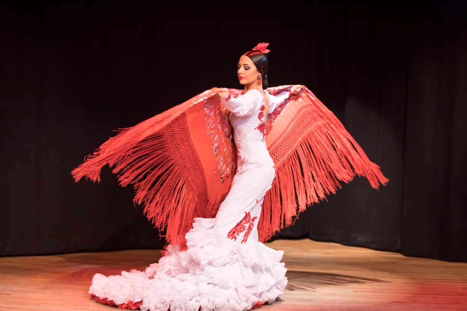 La Emi flamenco dancer on stage in white dress holding a red shawl
