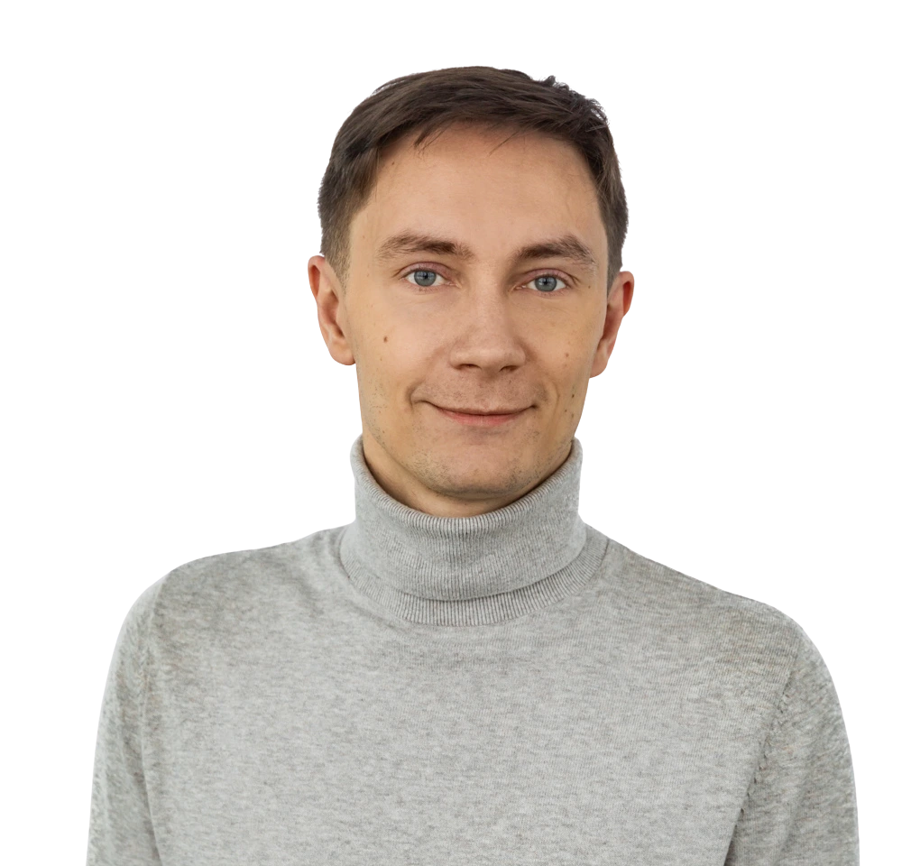 Man with short brown hair wearing a light gray turtleneck sweater, smiling gently, on a plain background.