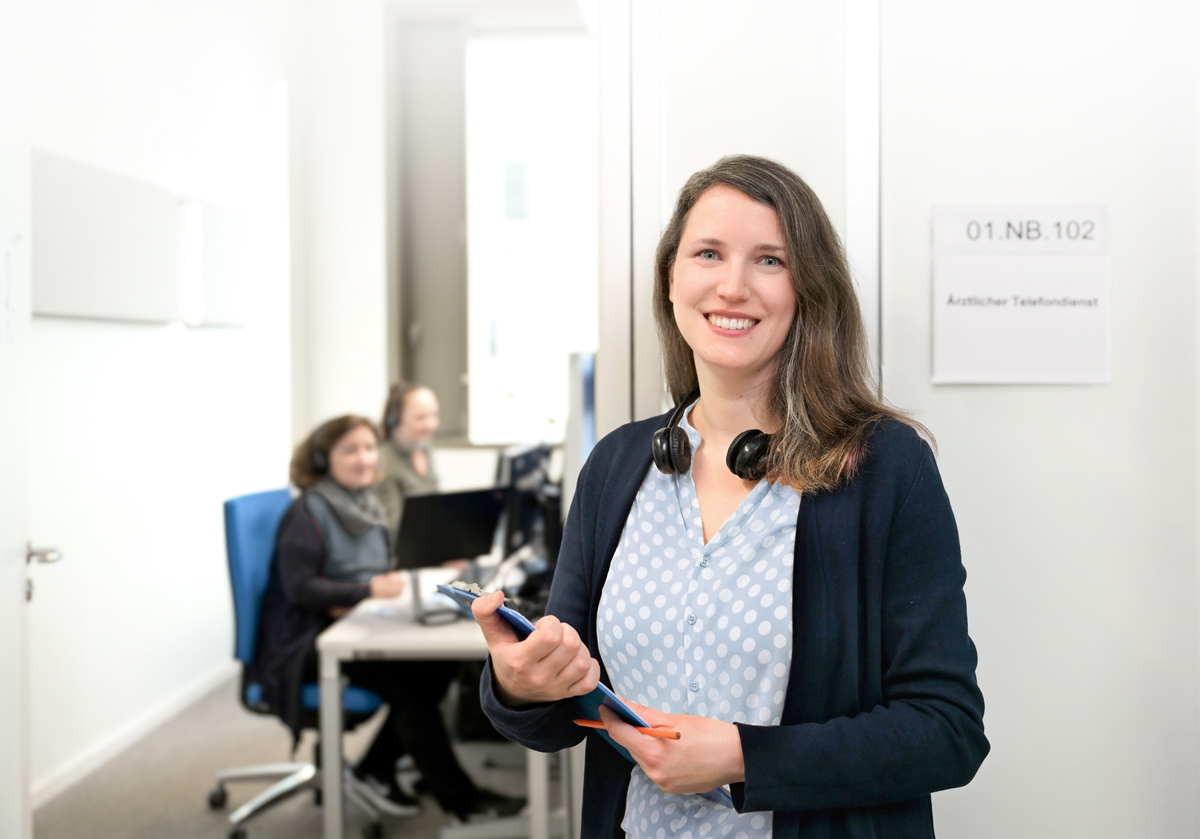 Eine Frau mit Kopfhörern und braunen Haaren steht in einem Büroumfeld