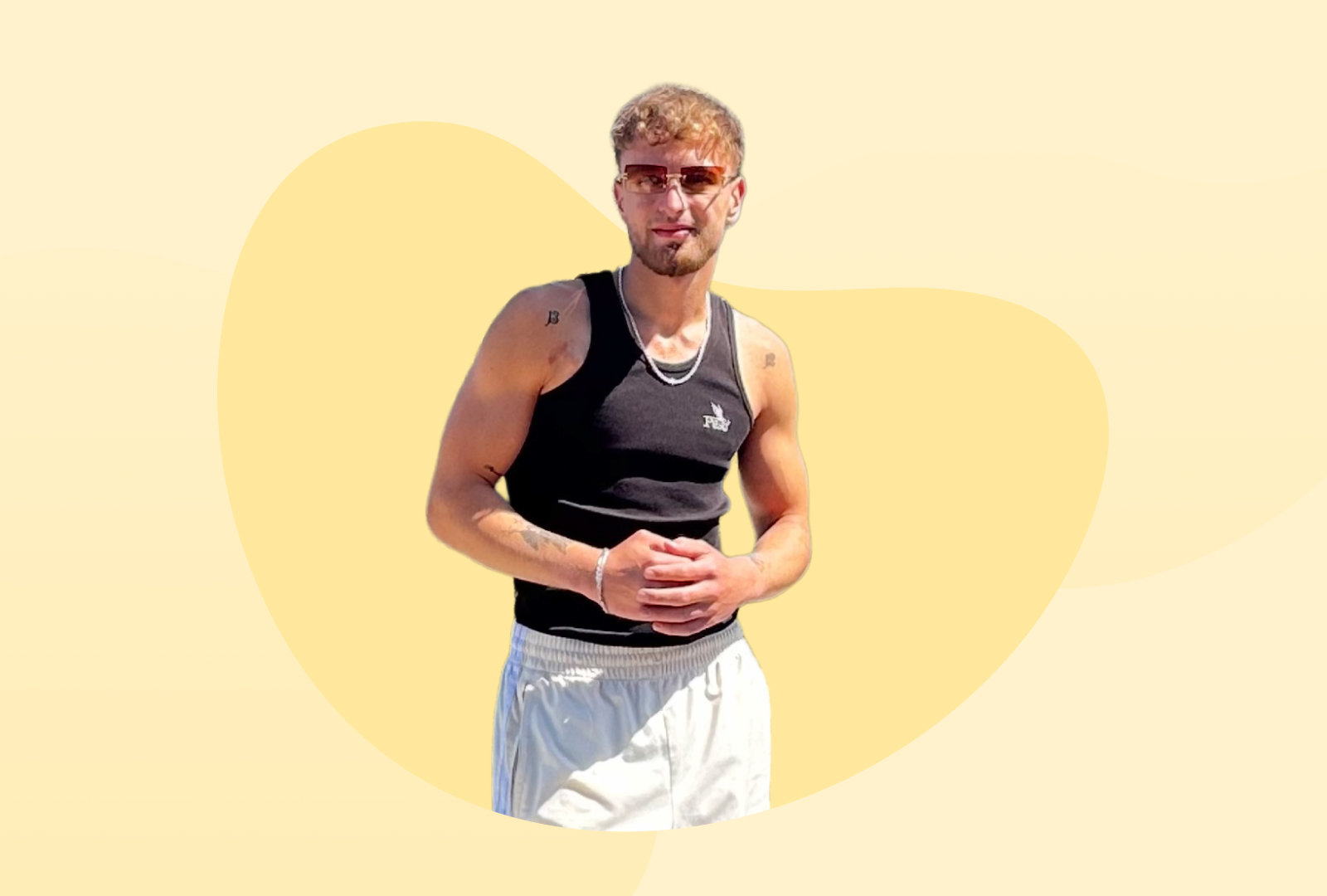 Ein junger Mann mit Sonnenbrille und schwarzem Tanktop lächelt in die Kamera.