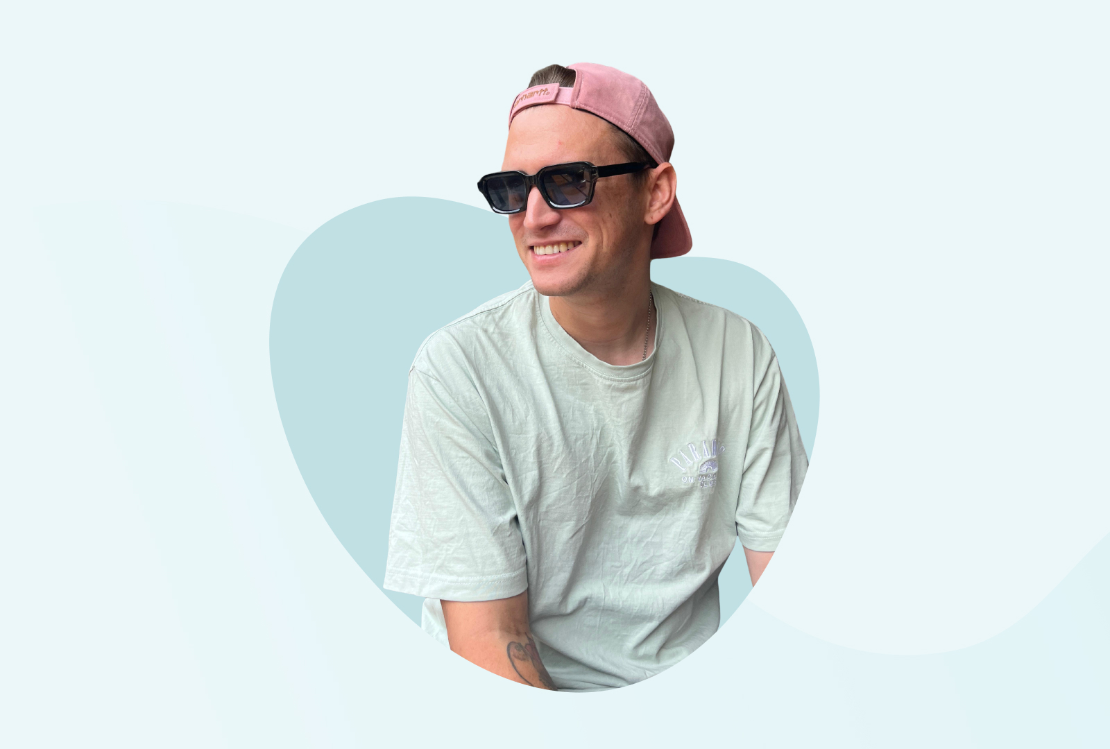 Tim trägt eine schwarze Sonnenbrille sowie altrosa-farbenes Cap und lächelt in die Kamera.