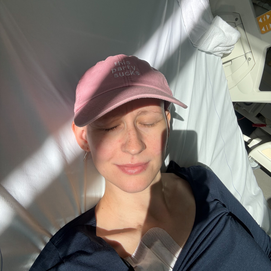 Jana trägt ein rosa Cap und hat die Augen geschlossen, während die Sonne durch das Krankenzimmerfenster in ihr Gesicht scheint.