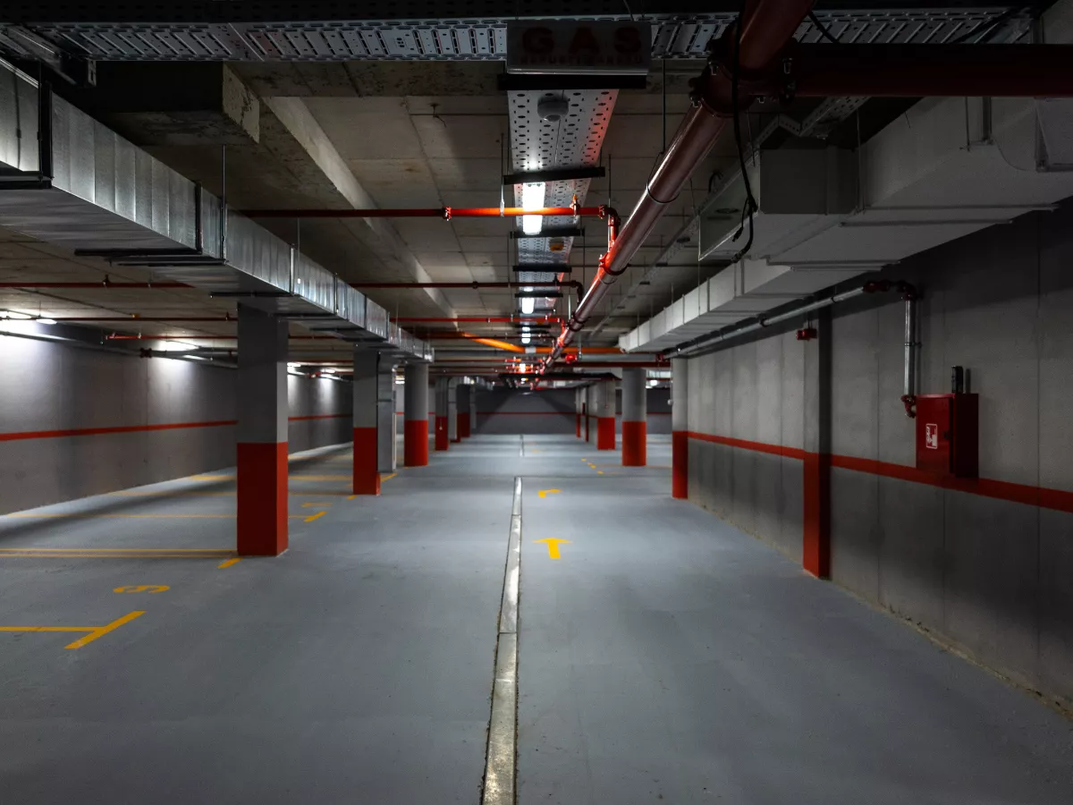 Empty underground parking garage with grey floors, red columns, and yellow directional arrows.
