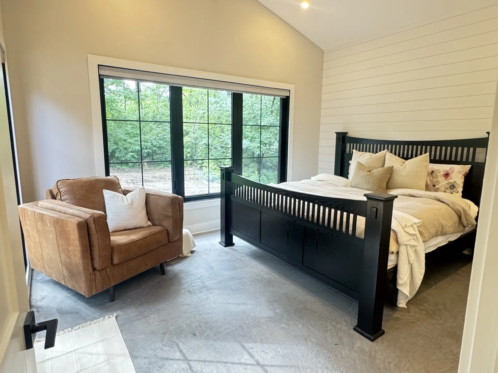 Primary bedroom with a vaulted ceiling, shiplap wall and large black-framed windows