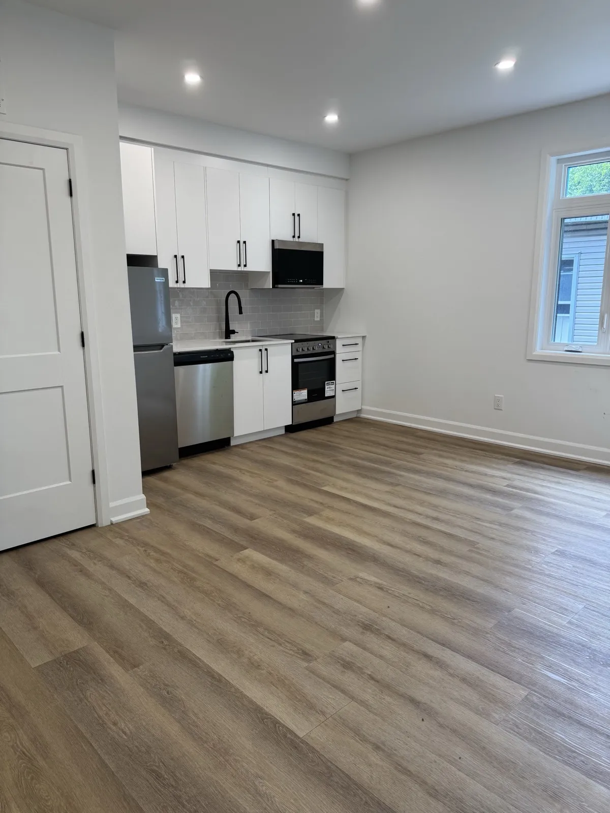 Open kitchen and living area in one of the eight units with white cabinets and vinyl plank flooring