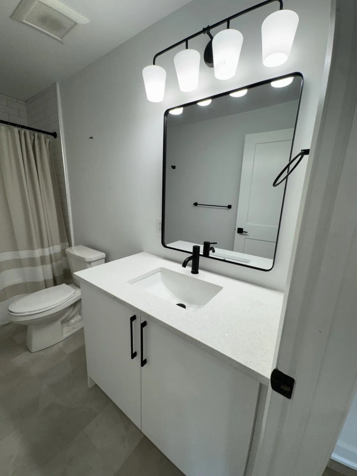 Unit bathroom vanity with black fixtures, a black-framed mirror and a four-light fixture