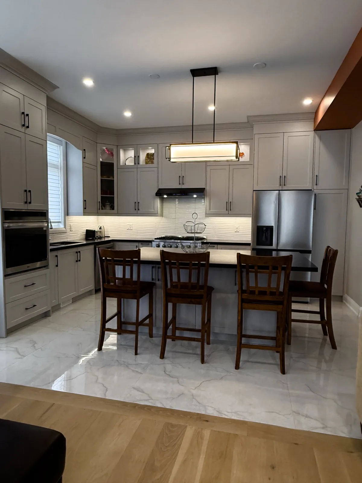 Custom home kitchen with grey Shaker cabinets, black quartz island and marble-look porcelain floor