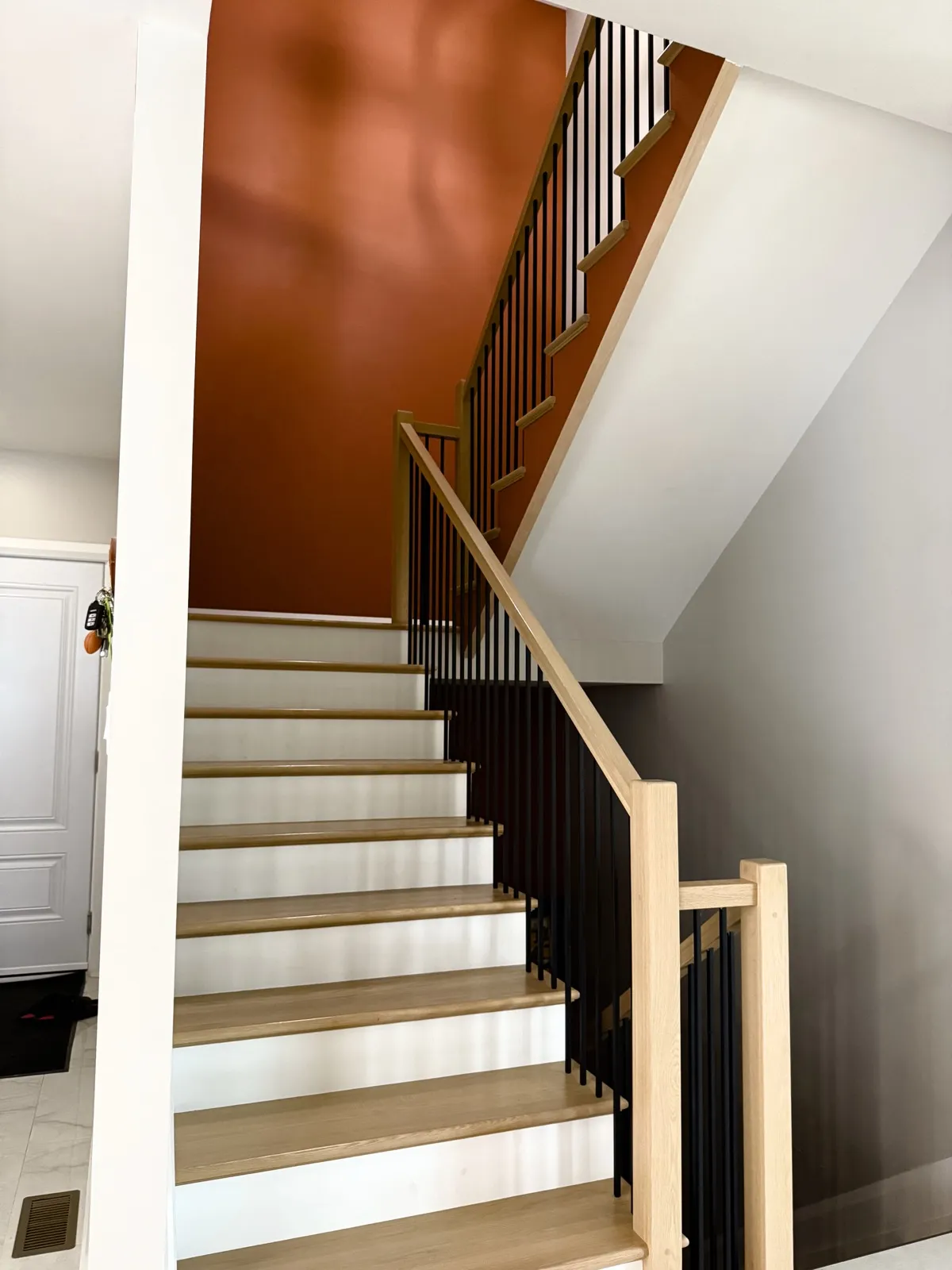 Staircase with oak treads, white risers and black metal spindles against a rust accent wall