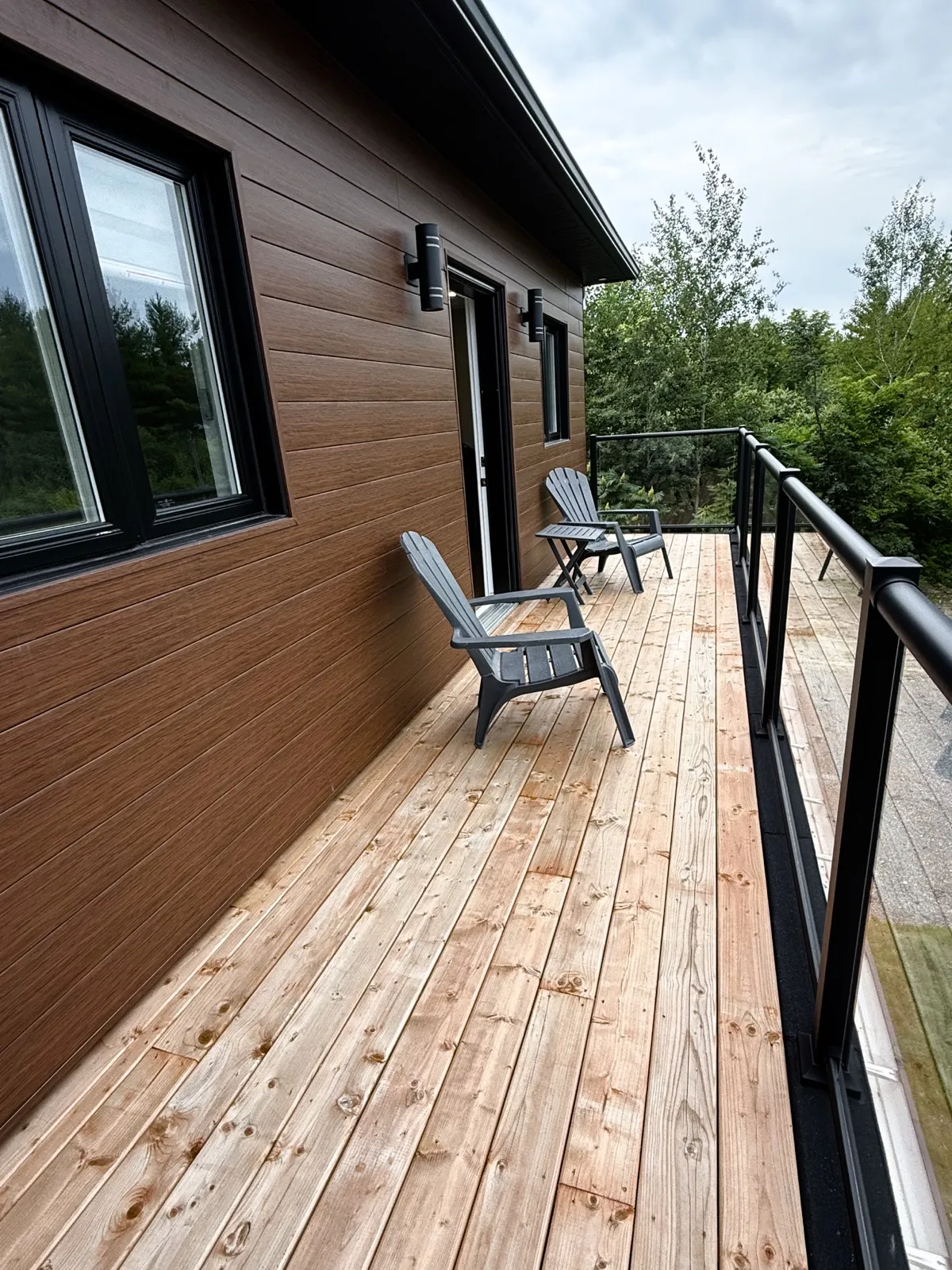 Upper-floor rear balcony with a cedar deck, glass railing and cedar-tone siding