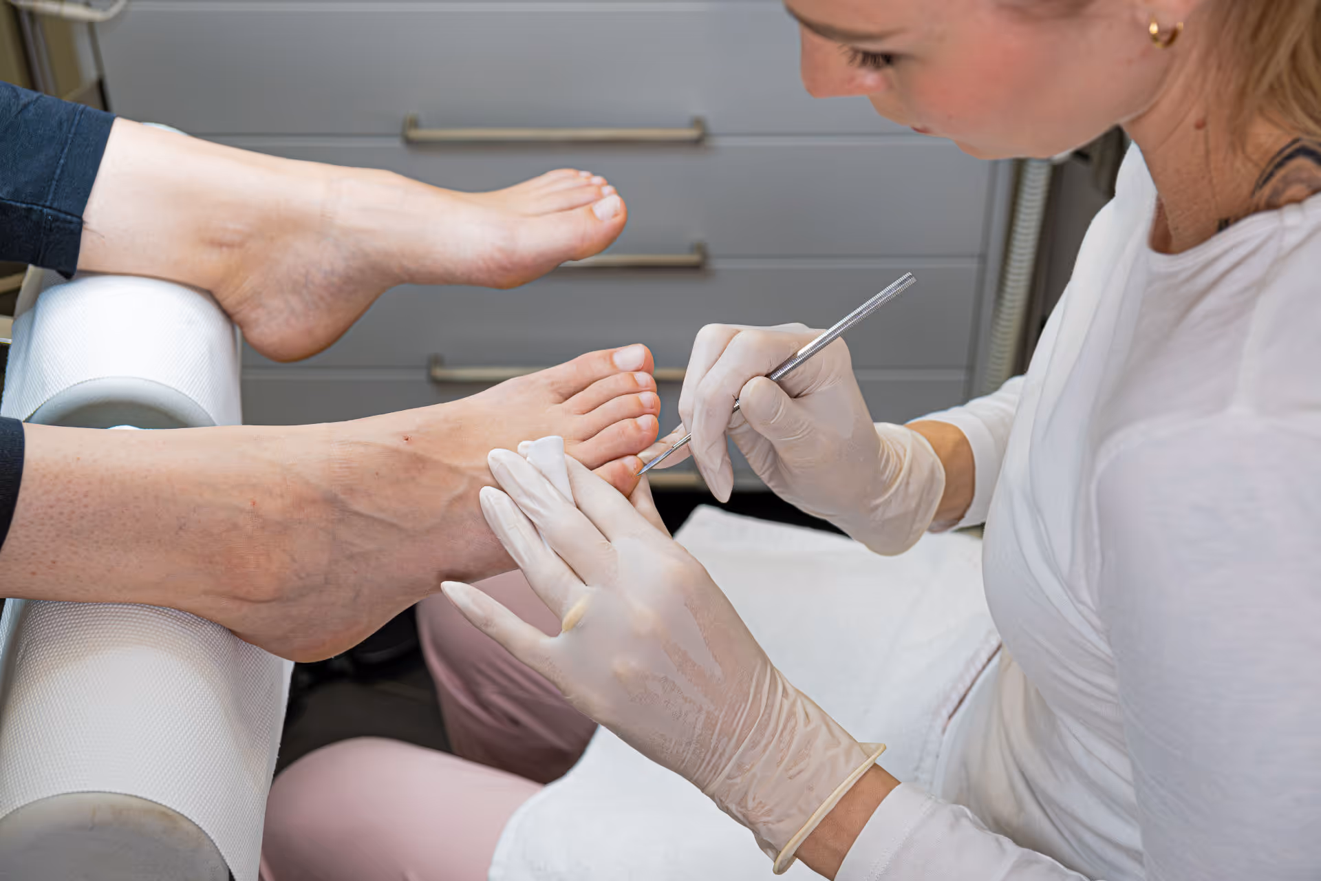 Podologin behandelt die Zehen eines Kunden mit einer speziellen Nagelpflege.