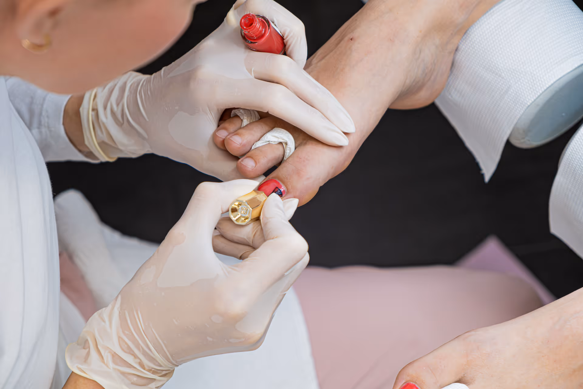 Podologin lackiert Zehennägel mit rotem Nagellack an einem Fuss, dabei trägt sie Handschuhe.
