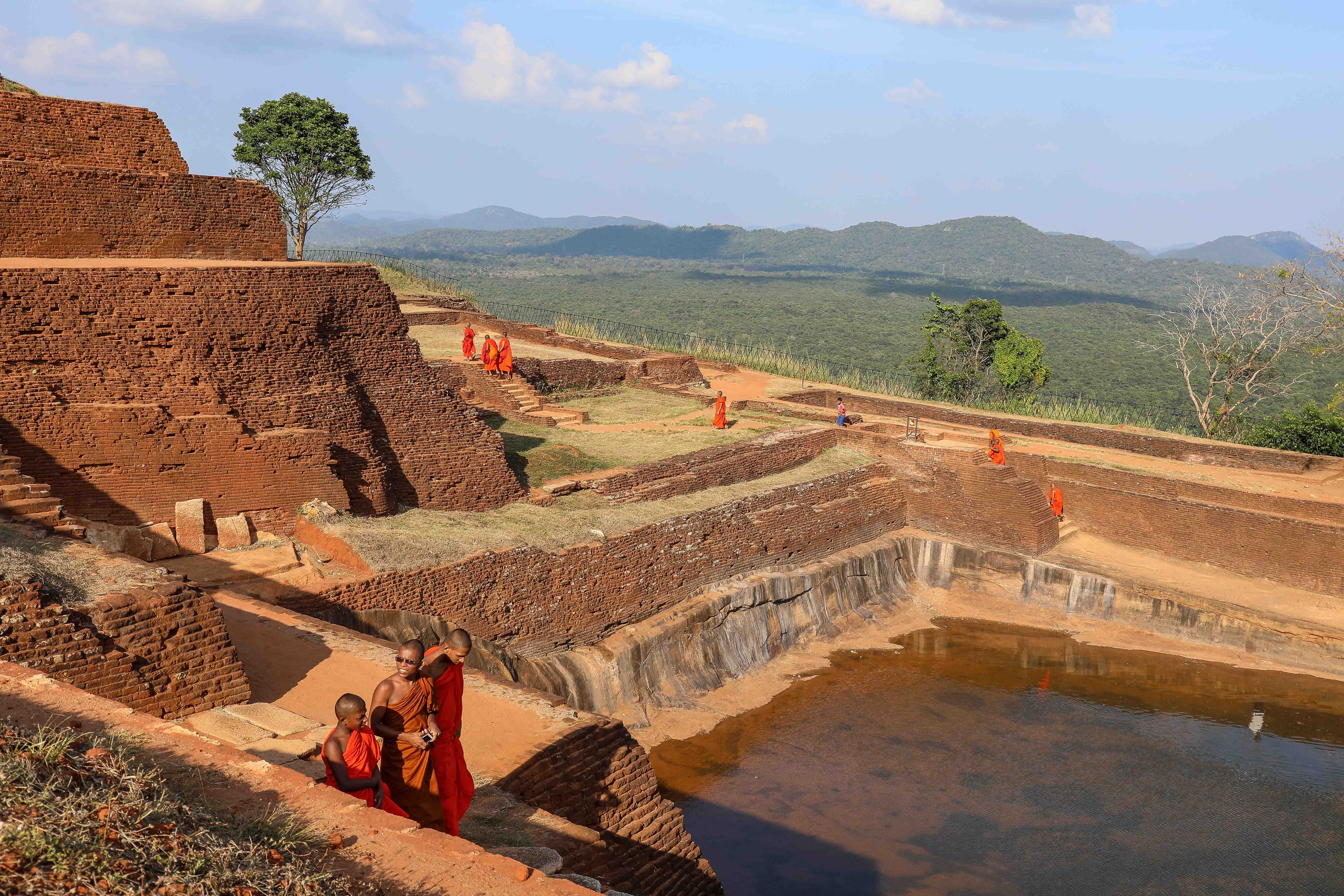 Buddhist monks walking among ancient brick ruins on the summit of Sigiriya Rock Fortress