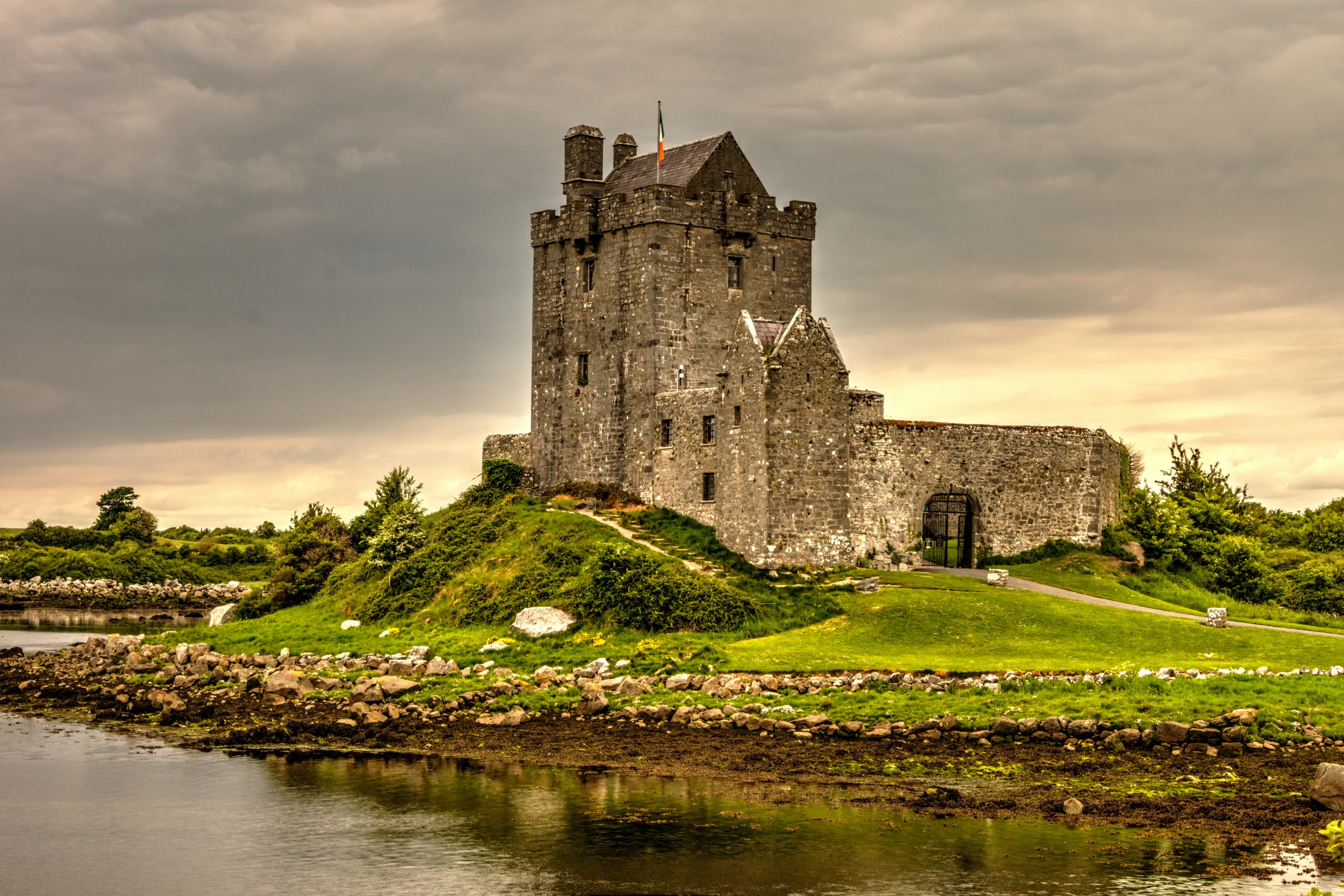 A stone tower castle on a grassy headland beside calm water in Ireland