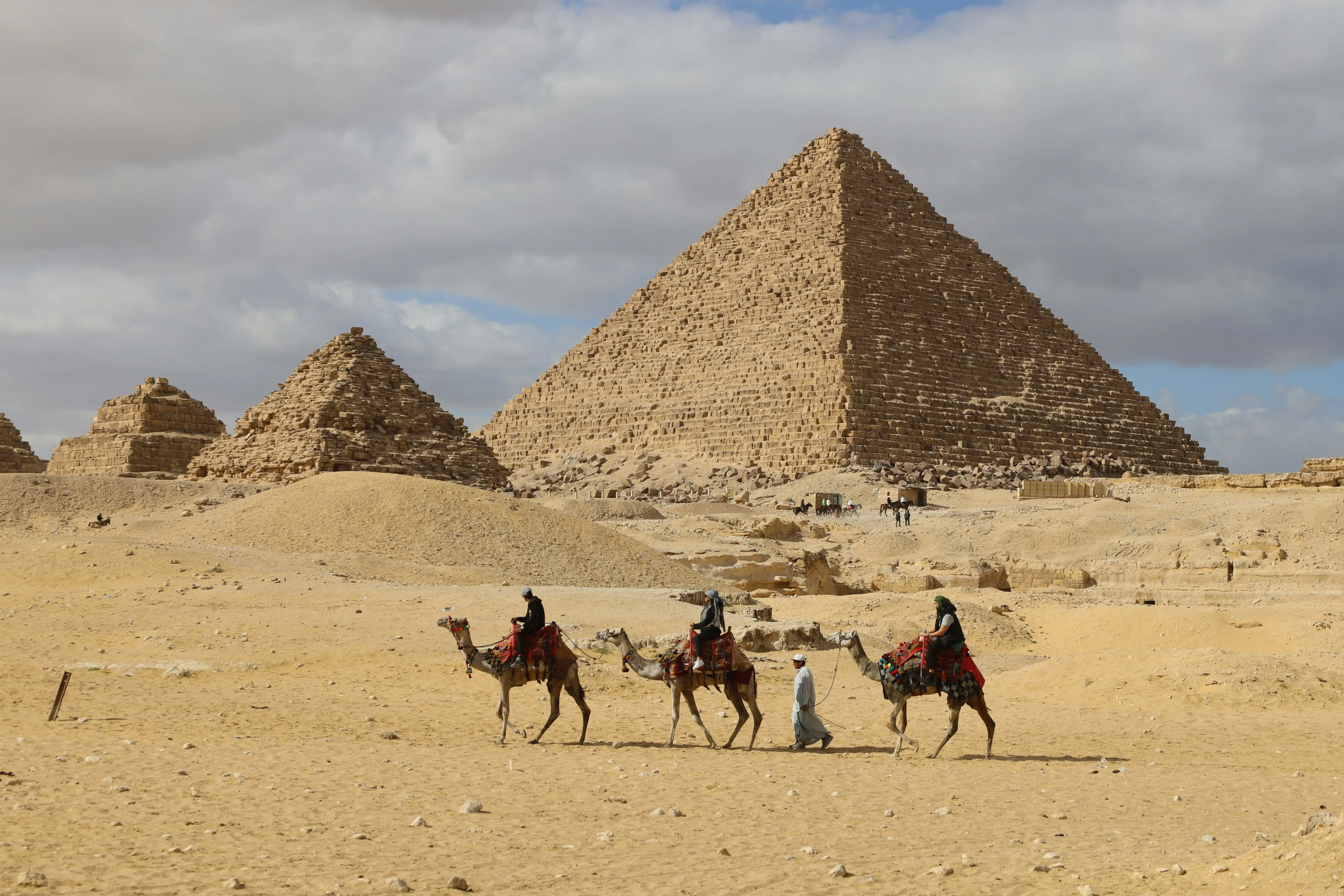 People riding camels across the desert in front of the Pyramids of Giza in Egypt