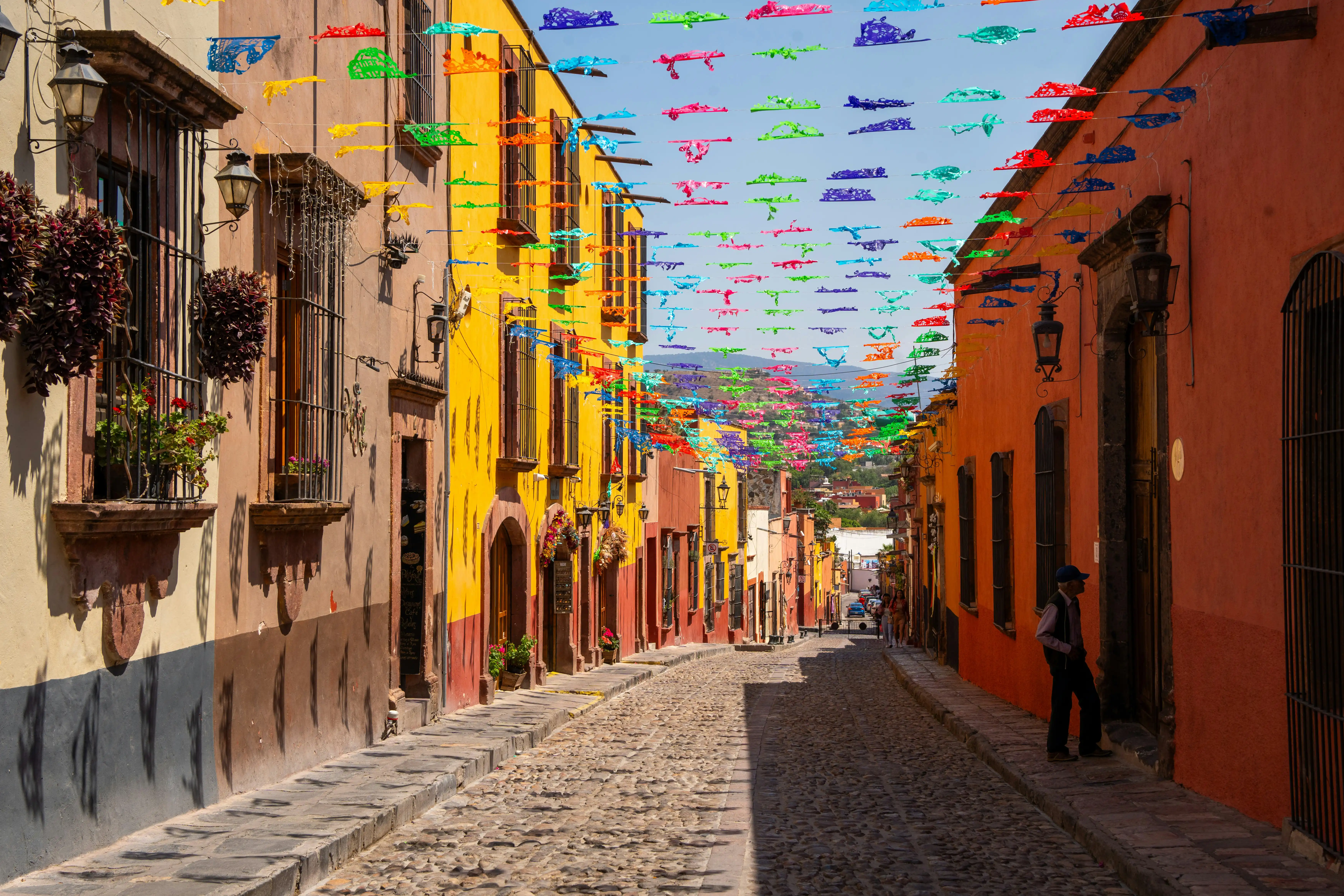 A cobblestone street lined with colourful buildings and bright papel picado bunting in Mexico