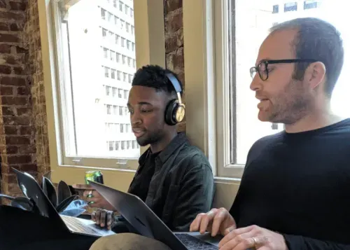 a couple of men sitting next to each other on laptops