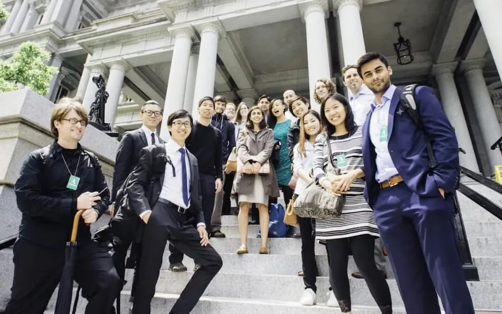 A diverse group of professionally dressed people smiling and standing on stone steps outside a classical building with large columns.