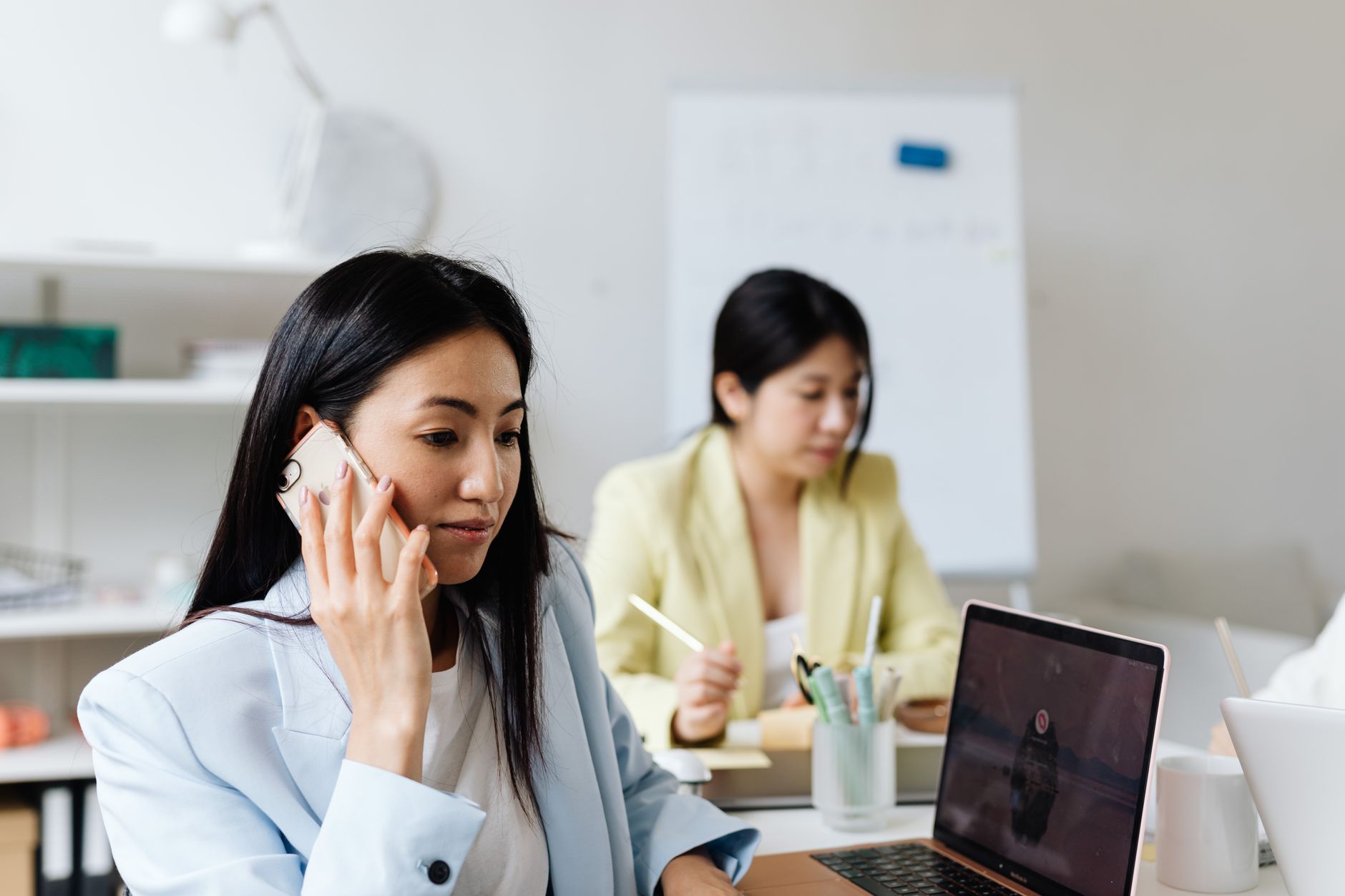Businesswoman using phone and laptop in a modern office setting.
