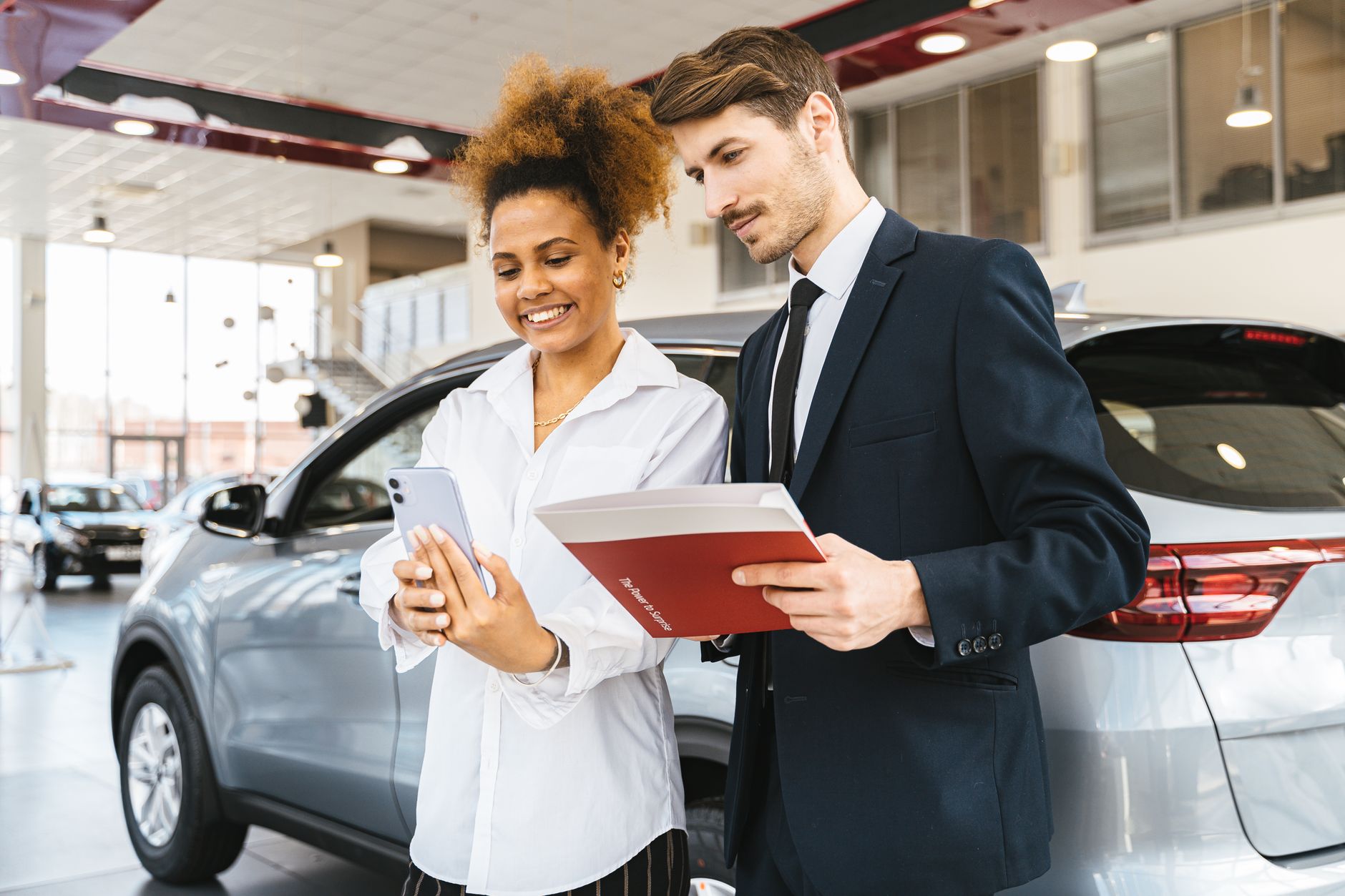 A woman and man smiling while reviewing details at a car dealership.